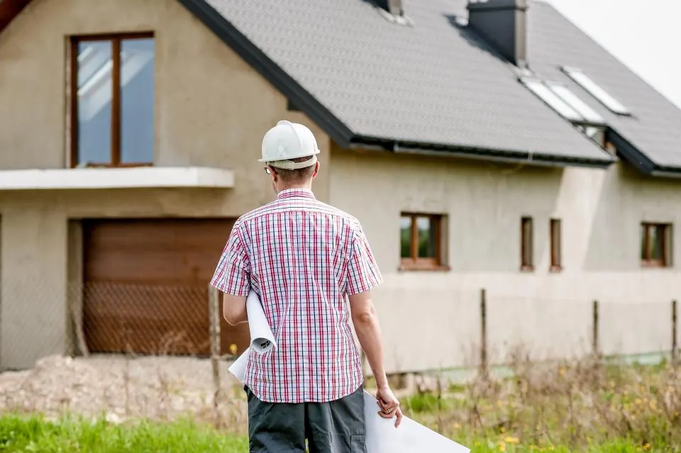 Un conseiller travaux, casque et plans à la main, devant une maison en chantier